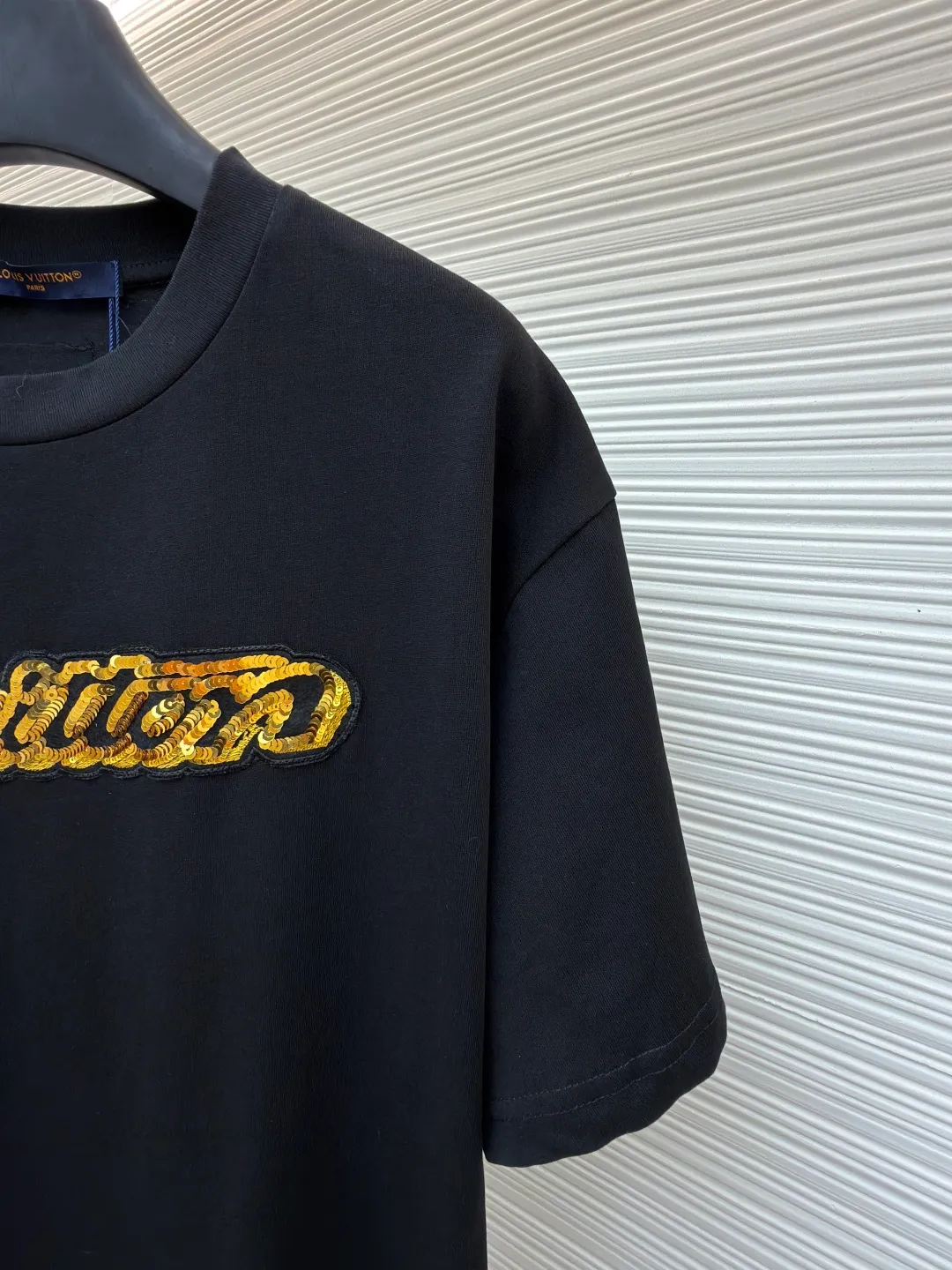LOUIS VUITTON cotton round neck embroidered Vuitton signature logo short sleeves ●Original version: purchased and developed for 12300 ●Item number: 1682273-A10 ●Fabric: cotton fabric ●Technology: embroidery production ●Color: black ●Version: fitted version ●Weight: about 295 grams ●Size: S-M-L-XL ●Description: This white short-sleeved T-shirt is made of high-count combed cotton fabric and has been treated with pre-washing technology. It has a soft and skin-friendly touch and is not easy to deform. The silhouette of the shirt is a loose shoulder design, which meets the needs of modern casual wear. The core decoration area on the chest uses hand-beading and bronzing technology, and uses metallic gold sequins and embroidery threads intertwined to outline a three-dimensional letter pattern. The sequins are layered and inlaid, and each one is manually positioned and fixed by craftsmen to ensure a regular texture and uniform gloss. The edges of the letters are sewn with matte silk thread to form a visual contrast between gold and matte, while reinforcing the decorative structure to avoid falling off during wear. The neckline uses double-needle hemming technology and is matched with ribbed cuffs of the same fabric. It is durable and fits the neck. The overall craftsmanship combines handicraftsmanship with modern clothing technology, and the details show exquisite texture. The overall wiring is straight and delicate, the fabric is comfortable and soft, and the color is consistent without color difference. It can be matched with the same style to create a fashionable look and control various occasions. Customized accessories, complete with three standards, same style for men and women!